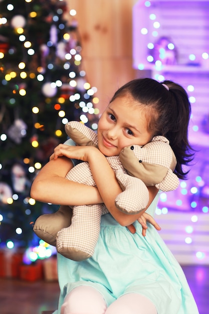 Nettes kleines Mädchen mit Bären nahe Weihnachtsbaum