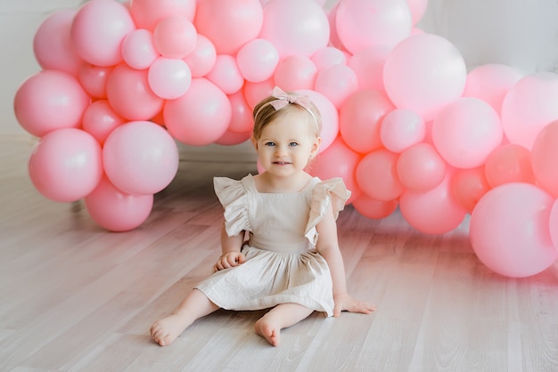 Nettes kleines Mädchen mit blondem Haar im beige Kleid, das mit rosa Ballons sitzt. Glückliche Momente, schönes Geburtstagskind. Babysitter.