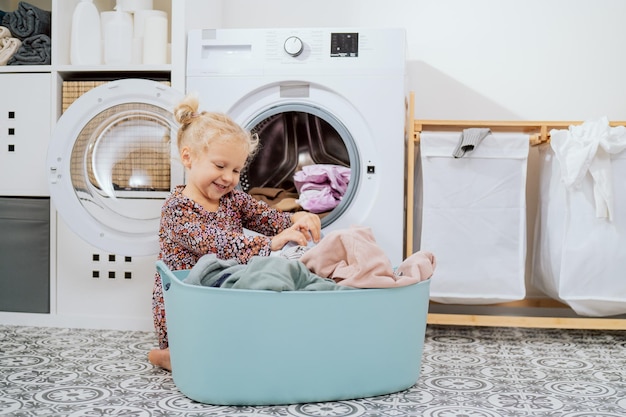 Nettes kleines Mädchen mit blonden Haaren, kleines Kind sitzt in der Waschküche des Badezimmers neben einer großen Schüssel voll