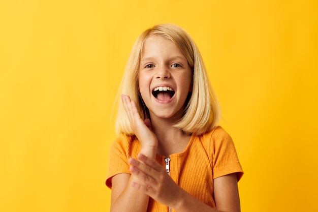 Nettes kleines Mädchen mit dem blonden Haar, das gelben Hintergrund aufwirft