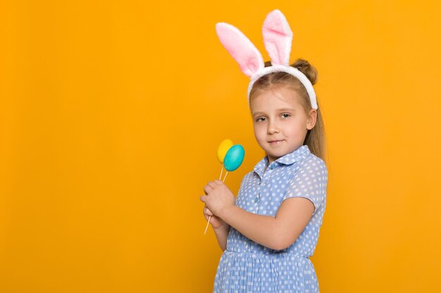 Nettes kleines Mädchen mit den Osterhasenohren, die bunte Eier halten