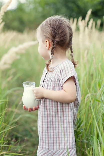 Nettes kleines Mädchen mit einem Krug Milch auf dem Feld an einem Sommertag, glückliche Kindheit.