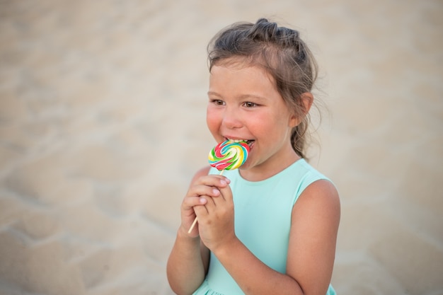 Nettes kleines Mädchen mit großem buntem Lutscher. Kind, das süßen Schokoriegel isst. Süßigkeiten für kleine Kinder. Sommerspaß im Freien.