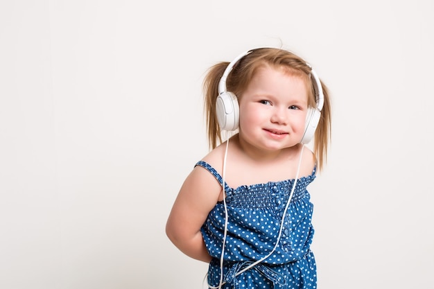 Nettes kleines Mädchen mit Kopfhörern, das Musik mit einem Tablet hört und auf weißem Hintergrund lächelt