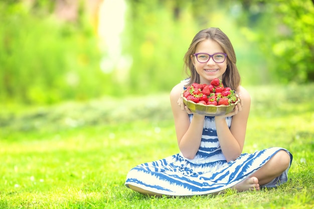 Nettes kleines Mädchen mit Schüssel voller frischer Erdbeeren Pre Teen Mädchen mit Zahnspangen