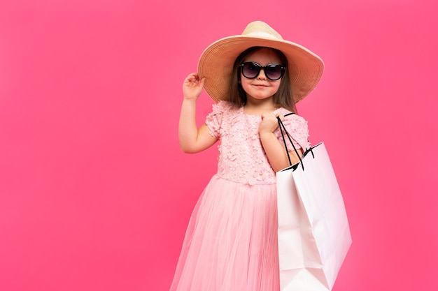 Nettes kleines Mädchen mit vielen Einkaufstüten im Kleid auf rosa Hintergrund