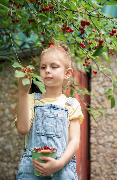 Nettes kleines Mädchen pflückt eine Kirsche von einem Baum im Kirschgarten