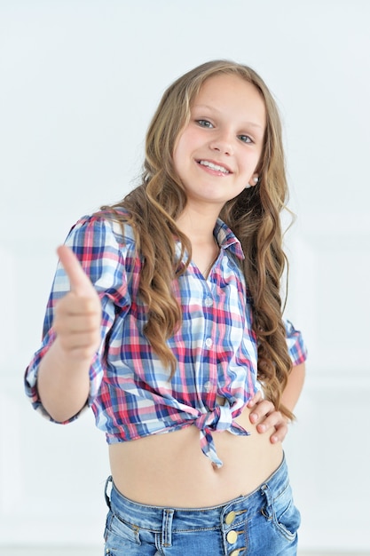 Foto nettes kleines mädchen posiert in hemd und jeans mit daumen nach oben im studio