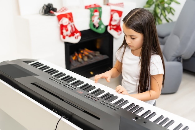 Nettes kleines Mädchen spielt Weihnachtsmelodie auf dem Klavier, frohe Weihnachtsfeier, glückliche saisonale Feiertage