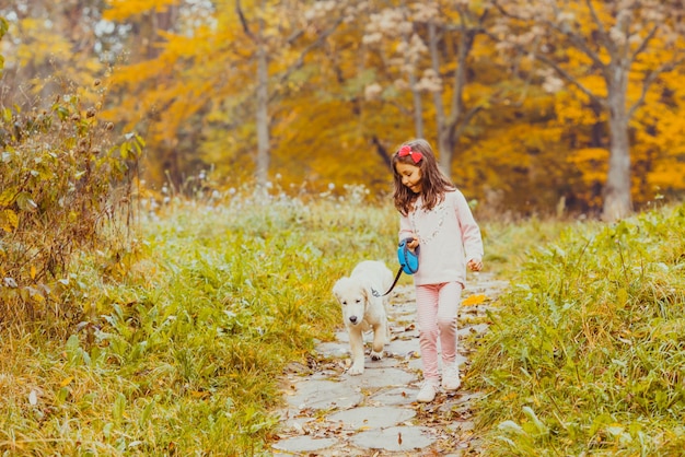 Nettes kleines Mädchen und Golden Retriever Hund an der Leine, die im Herbstpark spazieren geht