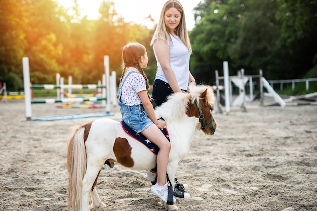 Nettes kleines Mädchen und ihre ältere Schwester, die draußen auf der Ranch mit Ponypferd genießen.