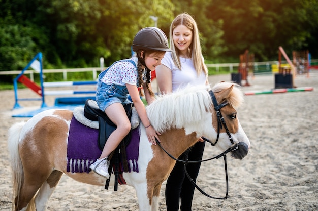 Nettes kleines Mädchen und ihre ältere Schwester, die draußen auf der Ranch mit Ponypferd genießen.