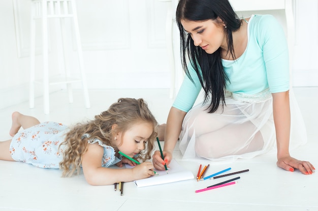 Nettes kleines Mädchen und ihre Mutter, die zusammen zuhause ein Bild zeichnet.