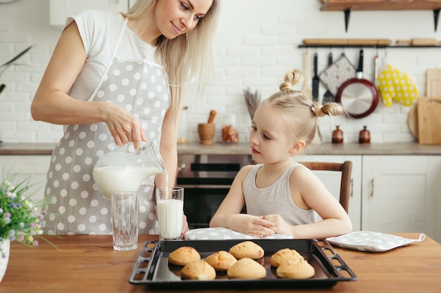 Nettes kleines Mädchen und Mutter essen frisch gebackene Kekse mit Milch in der Küche. Glückliche Familie. Tonisieren.