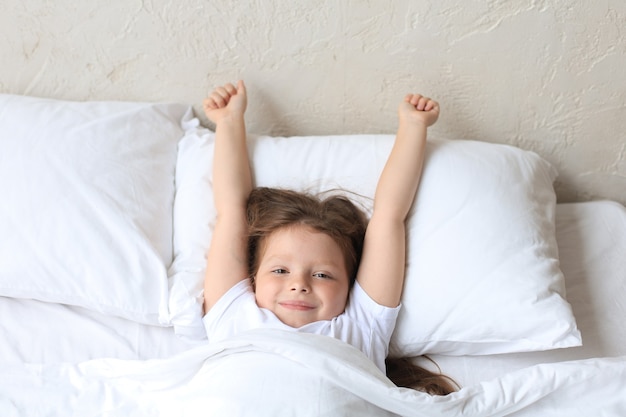 Nettes kleines Mädchen wachte auf und liegt im Bett.