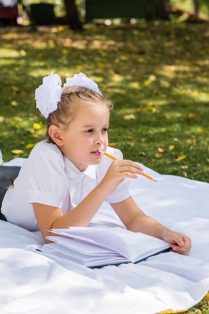 Nettes kleines Schulmädchen, das Hausaufgaben in einem sonnigen Herbstpark macht. Outdoor-Erziehung für Kinder. Zurück zum Schulkonzept. Vertikale Ansicht