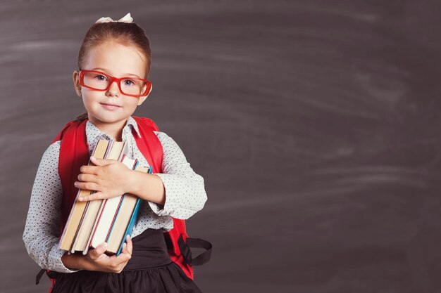 Nettes kleines Schulmädchen in Gläsern auf Tafelhintergrund