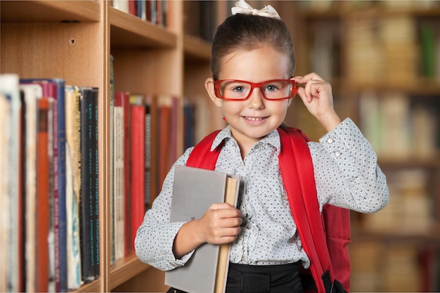 Nettes kleines Schulmädchen in Gläsern mit Buch im Hintergrund