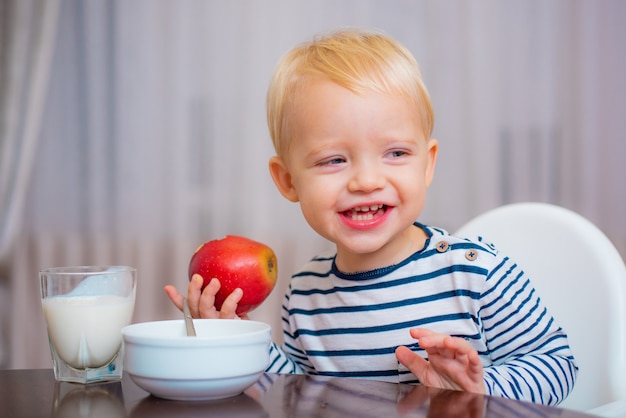 Nettes Kleinkind, das sein Essen isst, einen Apfel in der Hand hält und lächelt.