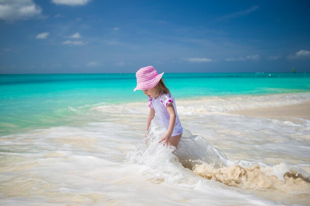 Nettes Kleinkindmädchen, das im seichten Wasser am exotischen Strand spielt