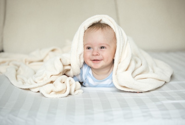 Nettes lächelndes Baby, das auf Bett unter weißer Decke liegt