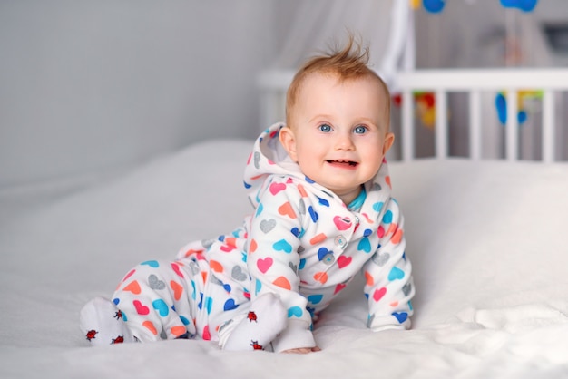 Nettes lächelndes Baby, das auf der weißen Decke auf Bett sitzt