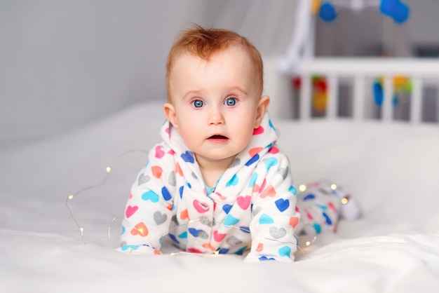 Nettes lächelndes Baby in einem stilvollen Kapuzenpulli, der auf einer weißen Decke liegt