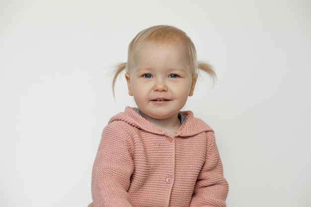 Nettes lächelndes Babymädchen lokalisiert auf Weiß Portrait von glücklichem Kleinkind im Studio Blondes behaartes Kind mit freudigem Gesichtsausdruck in rosa gestricktem Pullover Schönes Kinderkonzept Kindheit