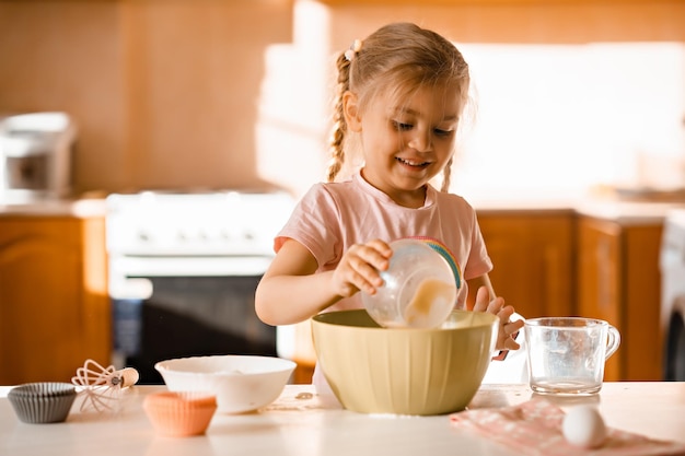 Nettes lächelndes kleines blondes Mädchen, das zu Hause Teig in der Küche kocht