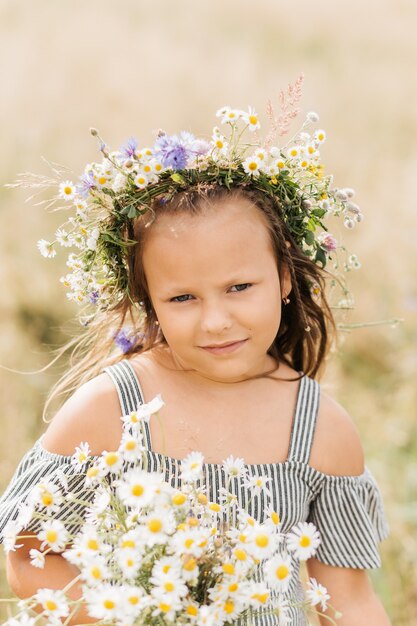 Nettes lächelndes kleines Mädchen mit Blumenkranz auf der Wiese. Porträt des entzückenden kleinen Kindes draußen.