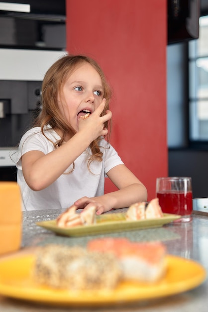 Nettes lächelndes kleines Mädchen mit Sushi auf weißem Hintergrund Kindermädchen, das Sushi isst und kommerzielles Konzept rollt