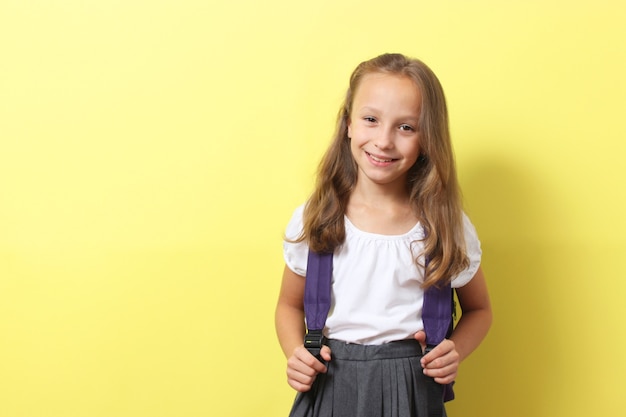 Nettes lächelndes Schulmädchen mit einem Schulrucksack auf einem farbigen Hintergrund