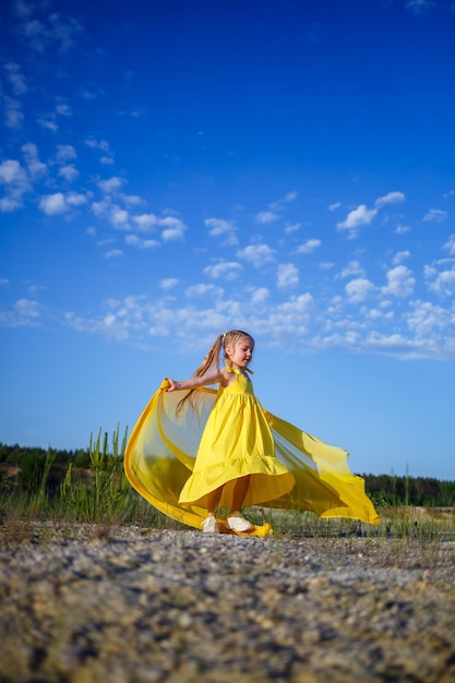 Nettes lockiges schönes blondes Mädchen in einem gelben Sommerkleid in der Natur