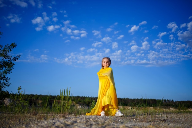 Nettes lockiges schönes blondes Mädchen in einem gelben Sommerkleid in der Natur