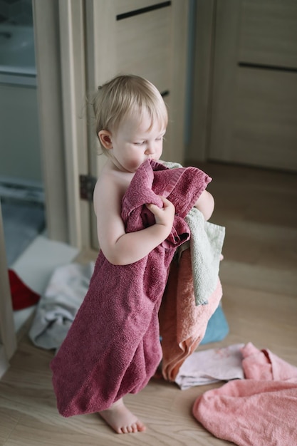 Nettes lustiges Baby, das zu Hause mit Stapel Handtüchern im Badezimmer spielt