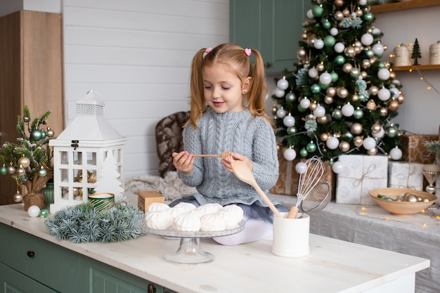 Nettes lustiges Mädchen sitzt auf Küchentisch am Weihnachtshaus