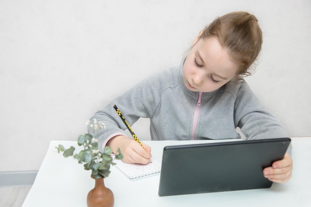 Nettes Mädchen am Tisch schreibt fleißig etwas vom Tablet Online-Lernen