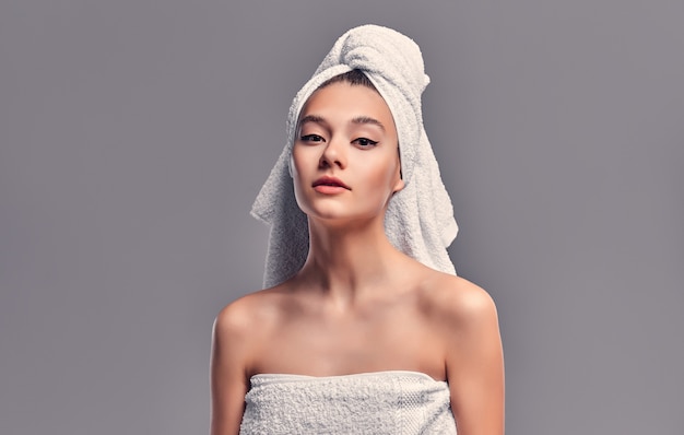 Nettes Mädchen auf grauem Hintergrund mit einem Handtuch auf dem Kopf nach einer Dusche. Hautpflege.