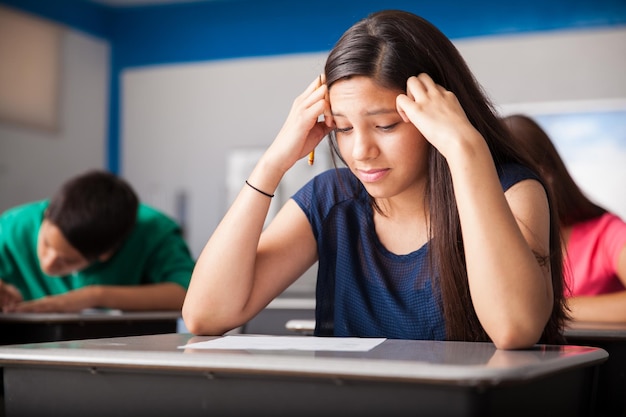 Nettes Mädchen, das besorgt aussieht, während es einen Test in einem Klassenzimmer macht