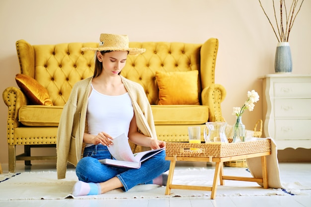 Nettes Mädchen, das Buch liest, das auf dem Boden im Wohnzimmer sitzt