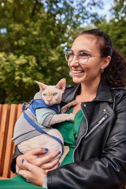 Nettes Mädchen, das eine pelzige Katze im Freien streichelt Sitzt auf einer Holzbank mit grünen Bäumen und Flusshintergrund Liebe zu den Tieren