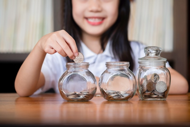 Nettes Mädchen, das Geldmünzen in Glas einsetzt und Geldkonzept spart