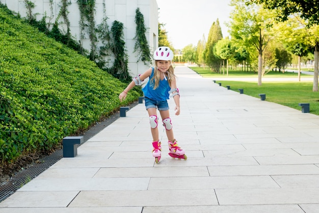 Nettes Mädchen, das lernt, Rollerblades auf öffentlichem Park am sonnigen Tag zu reiten