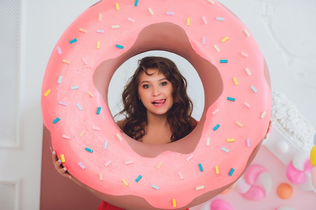 Nettes Mädchen, das mit rosa Donuts aufwirft, herumalbern, Dessert, schlechtes Essen, schaut in das Loch im Donut, hält Donuts durch die Augen