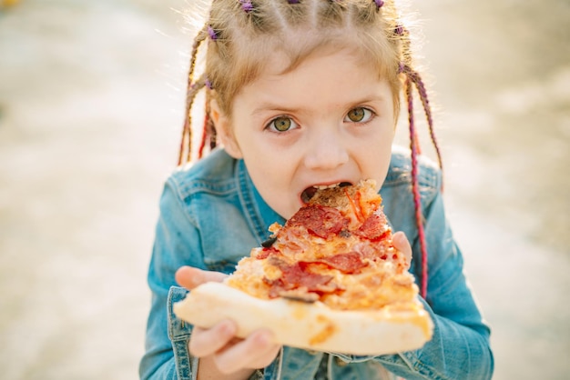 Nettes Mädchen, das Pizza isst. Fastfood für Kinder. Italienische Küche. Konzept der Kindheit.