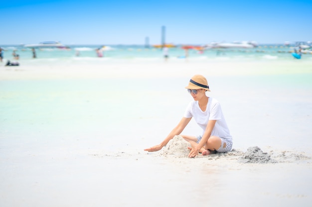 Nettes Mädchen, das Sand auf Strand für entspannende Zeit im Sommer auf blauem Himmel spielt