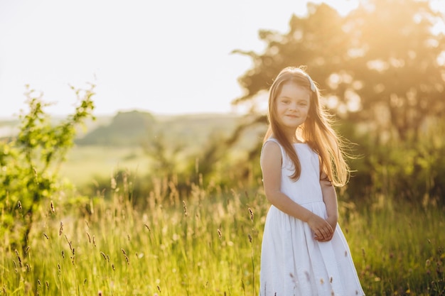 Nettes Mädchen, das weißes Kleid im grünen Feld hält