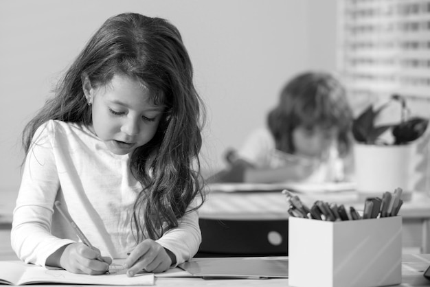 Nettes Mädchen der Kinder, das im Klassenzimmer in der Schule zeichnet