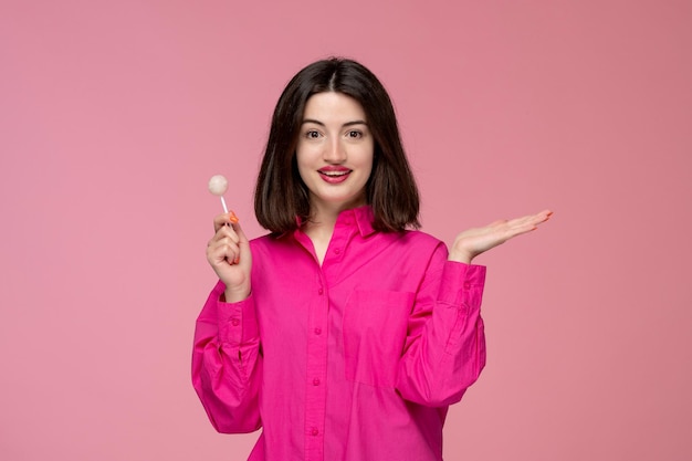 Nettes Mädchen hübsches entzückendes Mädchen im rosa Hemd mit dem roten Lippenstift, der Hände mit einer Süßigkeit winkt