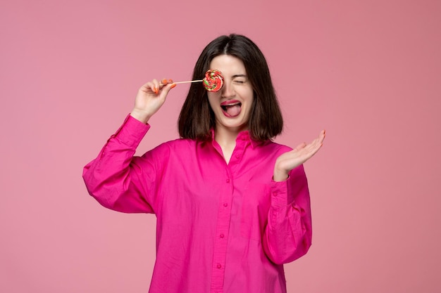 Nettes Mädchen hübsches junges schönes Brunettemädchen im rosafarbenen Hemd, das ein Auge mit Lutscher bedeckt